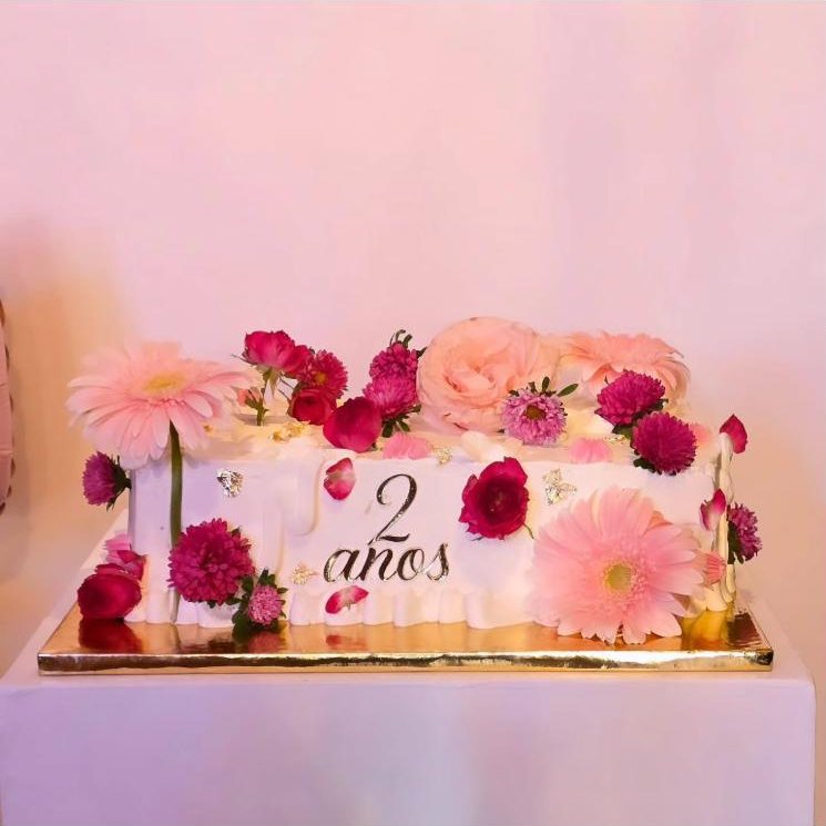 Bolo branco decorado com flores cor-de-rosa, feito para os 2 anos da loja